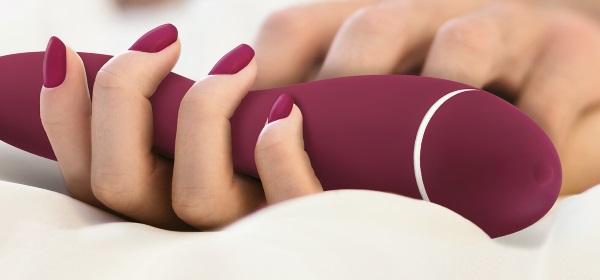 magenta vibrator in hands of woman lying in bed